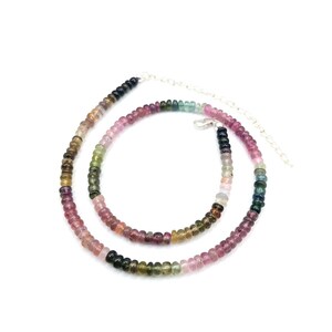 May include: A multi-colored gemstone necklace with a silver chain. The necklace is made of small, round beads in shades of pink, green, blue, and black.