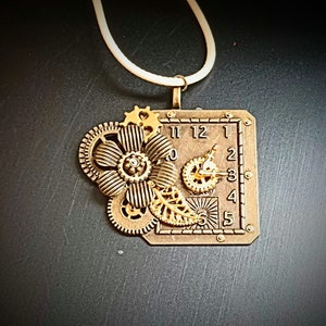 May include: A gold-toned steampunk necklace with a clock face, gears, and a flower design. The necklace is on a white cord.