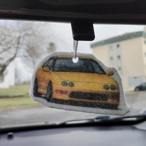 May include: A yellow car air freshener hanging from a rear view mirror. The car is a Honda CRX.