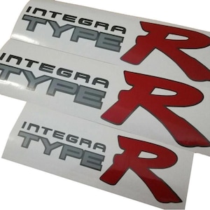 Può includere: Tre adesivi bianchi con le parole "Integra Type R" in lettere grigie e un logo "R" rosso.
