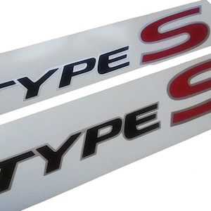 Puede incluir: Dos calcomanías blancas con letras negras y rojas. La calcomanía superior dice "TYPE S" en letras negras con una "S" roja. La calcomanía inferior dice "TYPE S" en letras negras con una "S" roja.