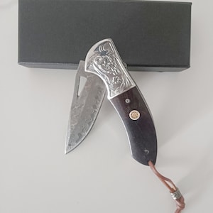 May include: A silver pocket knife with a dark wood handle and a decorative design. The knife has a small, ornate blade and a leather lanyard.