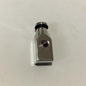 May include: A stainless steel bottle stopper with a rectangular body and a small, round ball in the centre. The top has a black rubber ring. The stopper is designed to fit into a bottle.