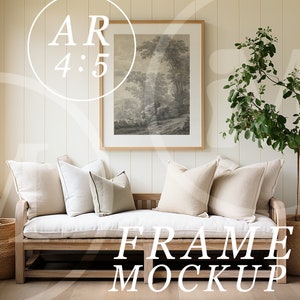 May include: A white framed picture with a black and white landscape print hangs on a light beige wall above a wooden bench with white cushions. A potted plant with green leaves stands to the right of the bench. The text "FRAME MOCKUP" is printed in white on the floor in front of the bench.