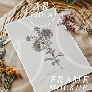 Op de afbeelding: Een ingelijste botanische print met een gedetailleerde grijswaarden illustratie van bloemen, met de tekst "Reine Marguerite" en "FRAME MOCKUP". De print wordt gepresenteerd op een neutrale ondergrond, omringd door gedroogde bloemen en groen.