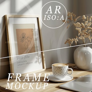 May include: A wooden frame mockup with a drawing of a flower inside. The frame is on a wooden table with a cup of coffee, a laptop, and a vase with dried flowers.