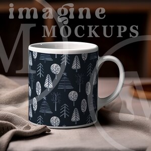 May include: White ceramic mug featuring a dark blue pattern of stylized trees in shades of gray and white. The mug has a white handle and rim. The words "imagine MOCKUPS" are visible in the background.