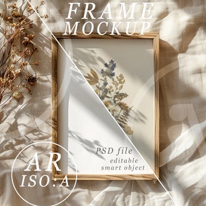 May include: A wooden frame mockup with a white background and a dried flower arrangement inside. The frame is sitting on a beige fabric surface with the text "FRAME MOCKUP" above the frame and "PSD file editable smart object" below the frame.