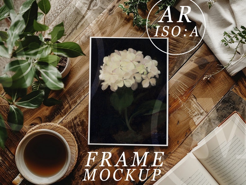 May include: A framed print of a white hydrangea flower on a black background. The frame is on a wooden table with a cup of coffee, a potted plant, and an open book.