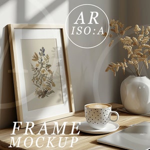 May include: A wooden frame mockup with a dried flower print inside. The frame is sitting on a wooden table with a cup of coffee, a vase with dried flowers, and a laptop.