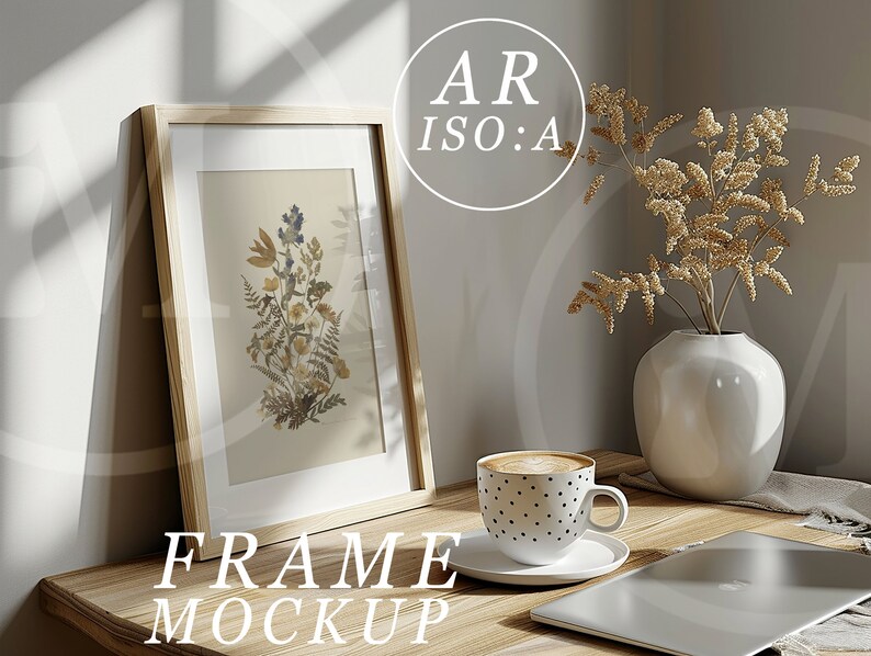 May include: A wooden frame mockup with a dried flower print inside. The frame is sitting on a wooden table with a cup of coffee, a vase with dried flowers, and a laptop.
