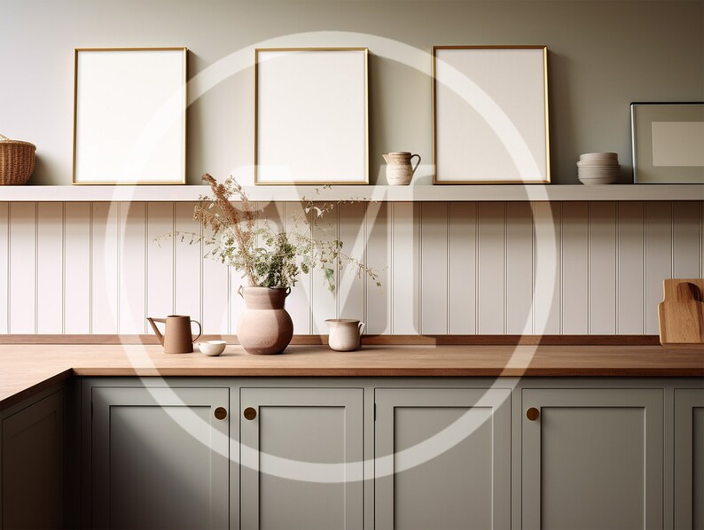 K&ouml;nnte beinhalten: K&uuml;cheninterieur mit drei gerahmten, leeren Kunstdrucken mit Goldrand &uuml;ber einer Arbeitsplatte. Die K&uuml;che hat salbeigr&uuml;ne Schr&auml;nke, eine Holz-Arbeitsplatte und ein Regal mit dekorativen Gegenst&auml;nden, darunter eine Vase mit Trockenblumen.