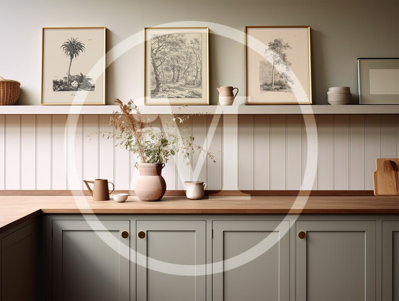K&ouml;nnte beinhalten: K&uuml;cheninterieur mit gerahmten botanischen Drucken, einer Vase mit Trockenblumen und verschiedenen Keramikkr&uuml;gen und -schalen. Die Schr&auml;nke sind in einem ged&auml;mpften Gr&uuml;n gehalten, mit Holz-Arbeitsplatten und goldenen Beschl&auml;gen.