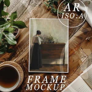 May include: A framed painting of a woman in a long dress standing in a room with a wooden chest. The painting is on a wooden table with a cup of coffee and a book. The text "FRAME MOCKUP" is below the painting.