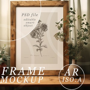 May include: A framed botanical print with a wooden frame, displayed on a wooden table. The print features a detailed illustration of flowers. The text "PSD file editable smart object" is visible on the frame. A small potted plant and a vase with flowers are on the table.