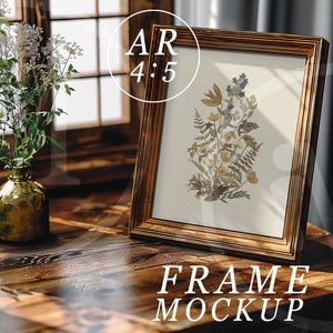K&ouml;nnte beinhalten: Ein Holzbildrahmen mit goldener Oberfl&auml;che steht auf einem Holztisch. Der Rahmen enth&auml;lt einen Druck von gepressten Blumen und Farnen. Der Text "FRAME MOCKUP" ist unter dem Rahmen gedruckt.