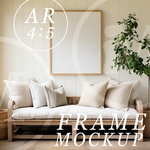 May include: A white couch with beige pillows sits in front of a large, empty picture frame with a wooden frame. A potted plant with green leaves stands to the right of the couch. The text "FRAME MOCKUP" is printed in white on the floor in front of the couch.