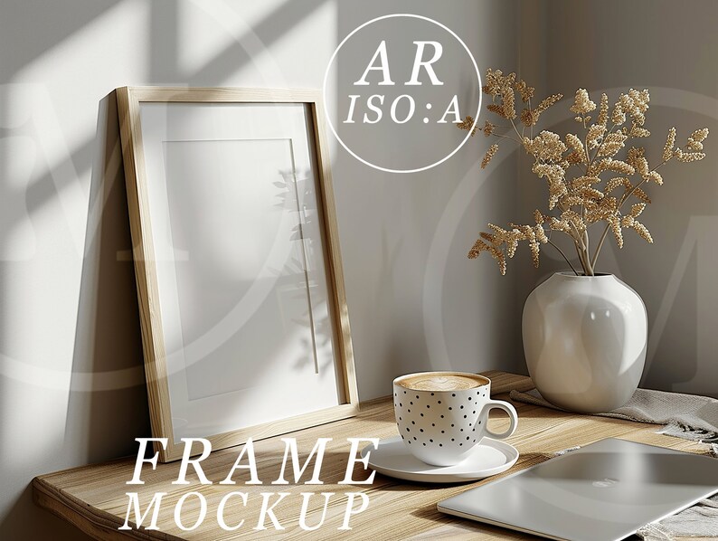 May include: A wooden frame mockup with a white mount and a white background. The frame is sitting on a wooden table with a cup of coffee, a vase with dried flowers, and a laptop.