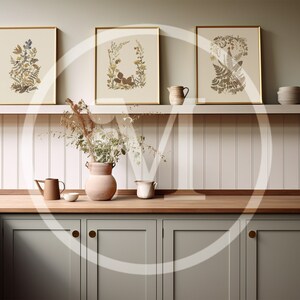K&ouml;nnte beinhalten: Drei gerahmte botanische Drucke mit goldenen Rahmen h&auml;ngen &uuml;ber einer Holz-Arbeitsplatte. Die Drucke zeigen detaillierte Illustrationen von Blumen und Bl&auml;ttern in Beige-, Braun- und Gr&uuml;nt&ouml;nen. Eine Vase mit Trockenblumen und andere dekorative Gegenst&auml;nde befinden sich auf der Arbeitsplatte.