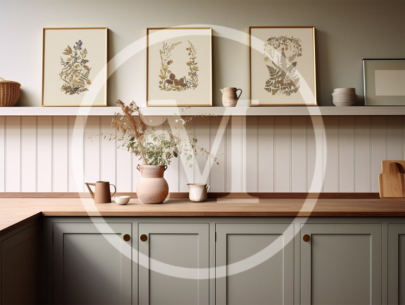 K&ouml;nnte beinhalten: Drei gerahmte botanische Drucke mit goldenen Rahmen h&auml;ngen &uuml;ber einer Holz-Arbeitsplatte. Die Drucke zeigen detaillierte Illustrationen von Blumen und Bl&auml;ttern in Beige-, Braun- und Gr&uuml;nt&ouml;nen. Eine Vase mit Trockenblumen und andere dekorative Gegenst&auml;nde befinden sich auf der Arbeitsplatte.
