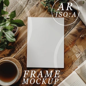 May include: A white frame mockup on a wooden surface with a cup of coffee, a book, and greenery. The text "FRAME MOCKUP" is written below the frame.