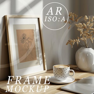May include: A wooden frame mockup with a black and white line drawing of a flower inside. The frame is sitting on a wooden table with a cup of coffee, a vase with dried flowers, and a laptop.