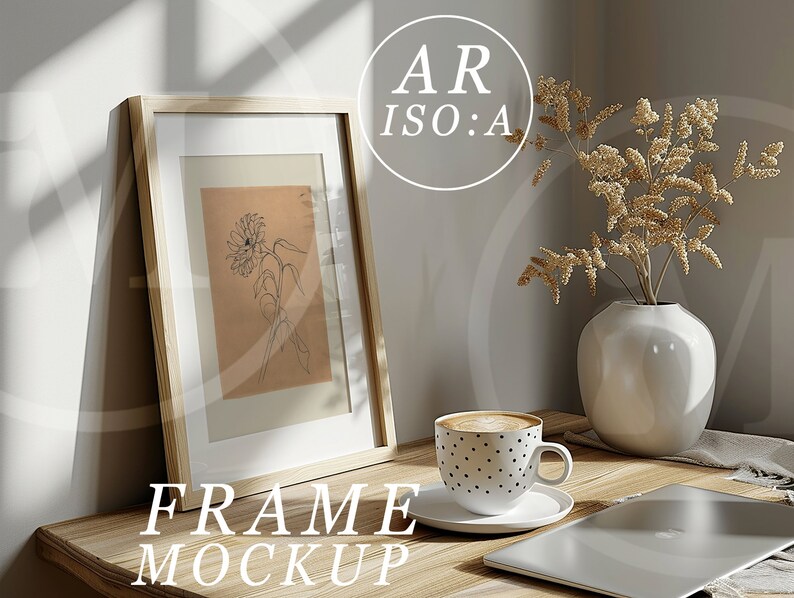 May include: A wooden frame mockup with a black and white line drawing of a flower inside. The frame is sitting on a wooden table with a cup of coffee, a vase with dried flowers, and a laptop.