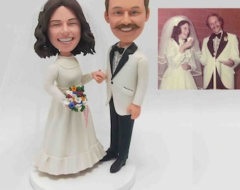 May include: A wedding cake topper featuring a bride and groom in a white dress and tuxedo. The bride is holding a bouquet of flowers and the groom is holding the bride's hand. The topper is based on a vintage wedding photo of the couple.