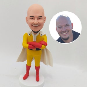 May include: A custom-made figurine of a person dressed as the superhero Saitama from the anime series One Punch Man. The figurine is made of clay and is painted in the character's signature yellow and red colours. The figurine is standing on a white base.