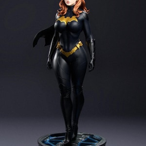 Op de afbeelding: Gedetailleerd beeld van Batgirl in een zwart en goud kostuum, cape en masker. Het figuur heeft rood haar en staat op een rond platform met blauwe accenten. Een verzamelobject.