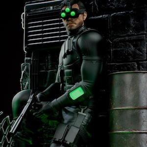 May include: A detailed statue of a character in a black tactical suit, wearing night vision goggles with three green lights. The figure is holding a pistol and is posed near a metal grate and barrels. The KC Studio logo is visible.
