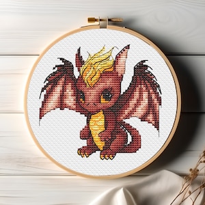 Può includere: Un drago ricamato con le ali, in tonalità di rosso e giallo, seduto su uno sfondo bianco. Il drago ha un aspetto carino e da cartone animato.