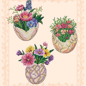Puede incluir: Arte de punto de cruz con tres arreglos florales. Las flores, en tonos rosa, morado, amarillo y azul, están en recipientes con forma de huevo y un jarrón. El fondo es de color melocotón claro con un borde decorativo.