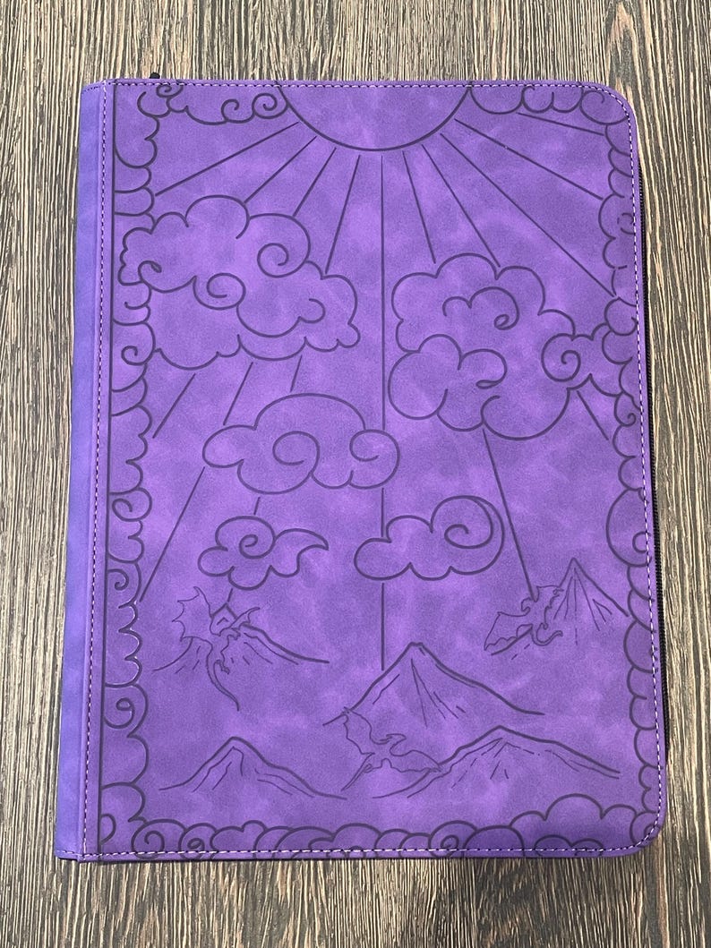 K&ouml;nnte beinhalten: Lila Rei&szlig;verschluss-Ordner mit einem gepr&auml;gten Design mit Sonne, Wolken und Bergen. Der Einband hat einen dekorativen Rand und eine gen&auml;hte Kante. Der Ordner besteht aus einem strukturierten Material.
