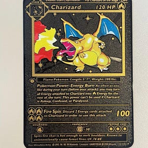 May include: A Charizard Pokémon trading card with a black background and gold accents. The card features a yellow and orange Charizard illustration with blue wings, flames, and text. The card reads "Charizard" and "120 HP".