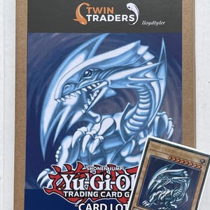 May include: A brown cardboard box featuring a Twin Traders logo and a large graphic of the Blue-Eyes White Dragon from Yu-Gi-Oh. A single Blue-Eyes White Dragon trading card in a protective sleeve is placed in the foreground of the box.