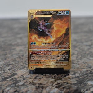 May include: A gold-colored Pokémon card featuring Origin Forme Palkia VSTAR. The card displays a character illustration with blue and purple accents against a fiery background. Text includes "Subspace Swell" and "Star Portal".