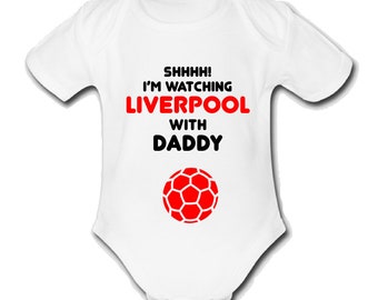 May include: White baby grow with a red football and the text "SHHHH! I'M WATCHING LIVERPOOL WITH DADDY" in black.