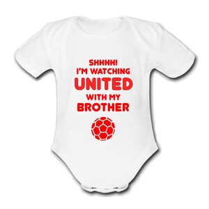 May include: White baby grow with red text that reads "Shhhh! I'm watching United with my brother" and a red football graphic.