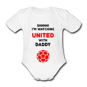 May include: White baby onesie with black text that reads "Shhhh! I'm watching United with Daddy" and a red soccer ball.