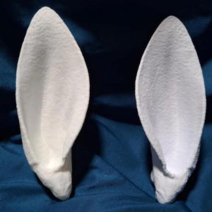 May include: Two white, 3D printed, rabbit ears. The ears are shaped like a traditional rabbit ear with a pointed tip and a rounded base. The ears are made of a smooth, white plastic.