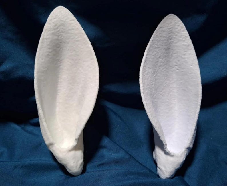 May include: Two white, 3D printed, rabbit ears. The ears are shaped like a traditional rabbit ear with a pointed tip and a rounded base. The ears are made of a smooth, white plastic.