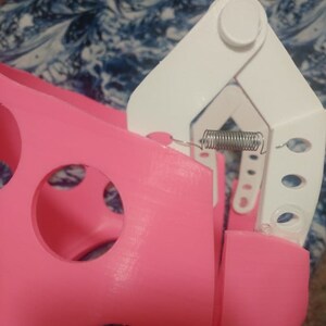 May include: A pink plastic object with a white plastic hinge and a metal spring. The object has several circular holes.