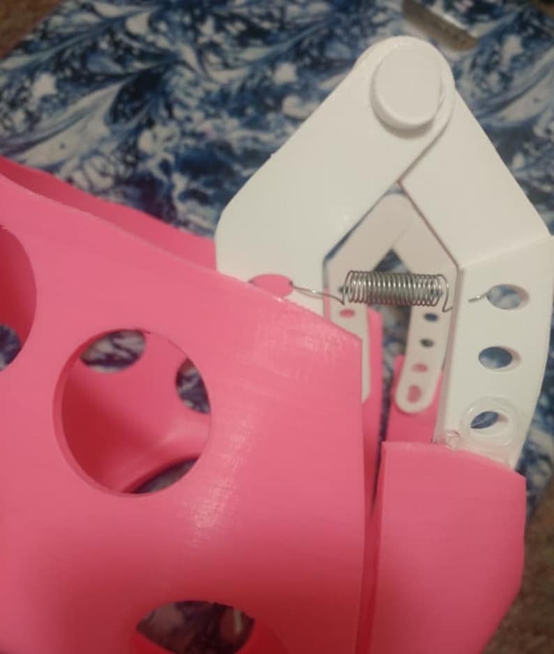 May include: A pink plastic object with a white plastic hinge and a metal spring. The object has several circular holes.