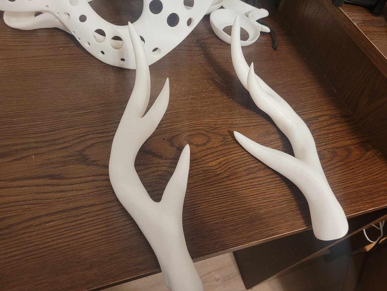 May include: Two white plastic deer antlers. The antlers are curved and have a smooth, polished finish.