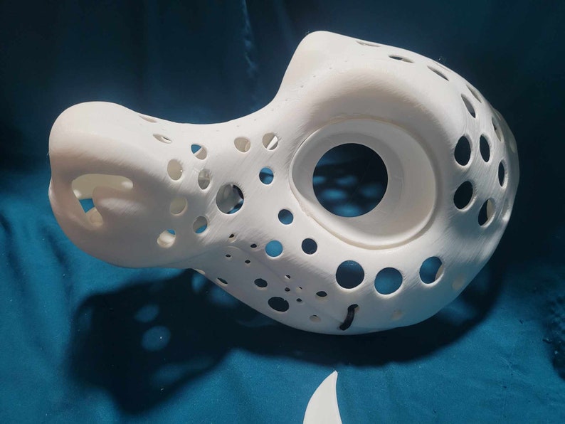 May include: White 3D printed mask with a large hole for the eyes and many smaller holes throughout the mask.