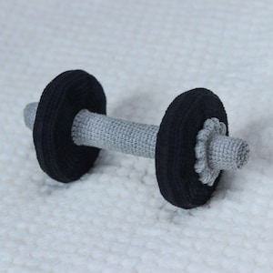 Op de afbeelding: Een grijs en zwart gehaakt halterspeelgoed. De halter is gemaakt van garen en heeft een realistisch ontwerp.