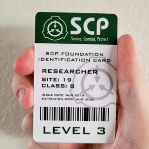 Peut inclure: Une carte d'identification blanche de la Fondation SCP avec du texte vert et noir. La carte indique "Chercheur, Site 19, Classe B, Niveau 3". La carte comporte un code-barres et les dates d'émission et d'expiration.