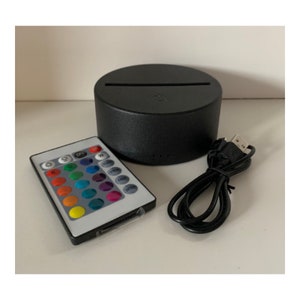 May include: A black round base with a white light strip, a black remote control with a white face and buttons for different colored lights, and a black USB cable.