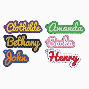 Peut inclure: Plusieurs étiquettes nominatives colorées. Les noms affichés sont Clothilde, Amanda, Bethany, Sacha, John et Henry. Chaque nom est dans une police et une couleur uniques, avec un contour contrasté.